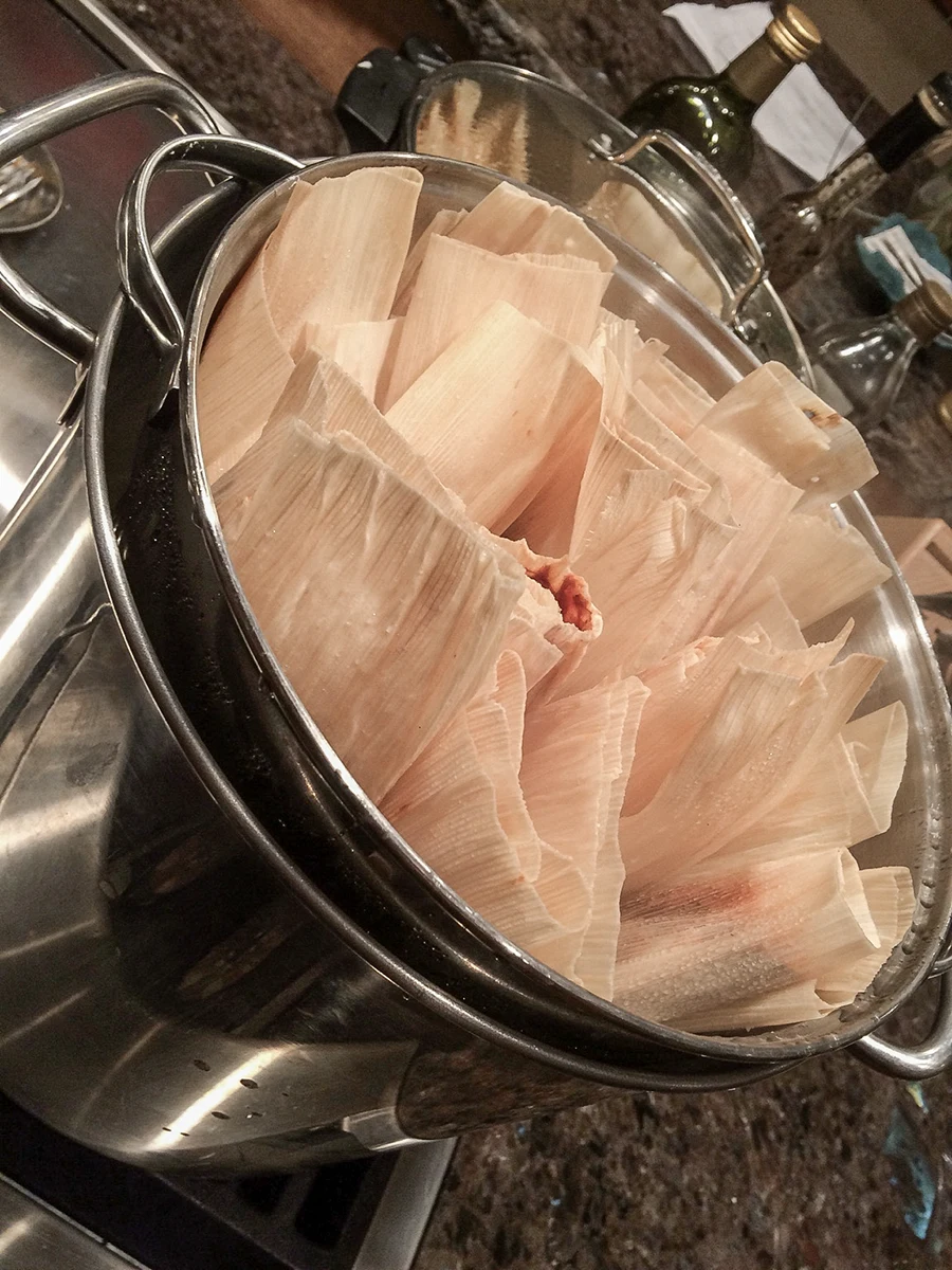 Corn-husk tamales arranged upright in a metal steamer.