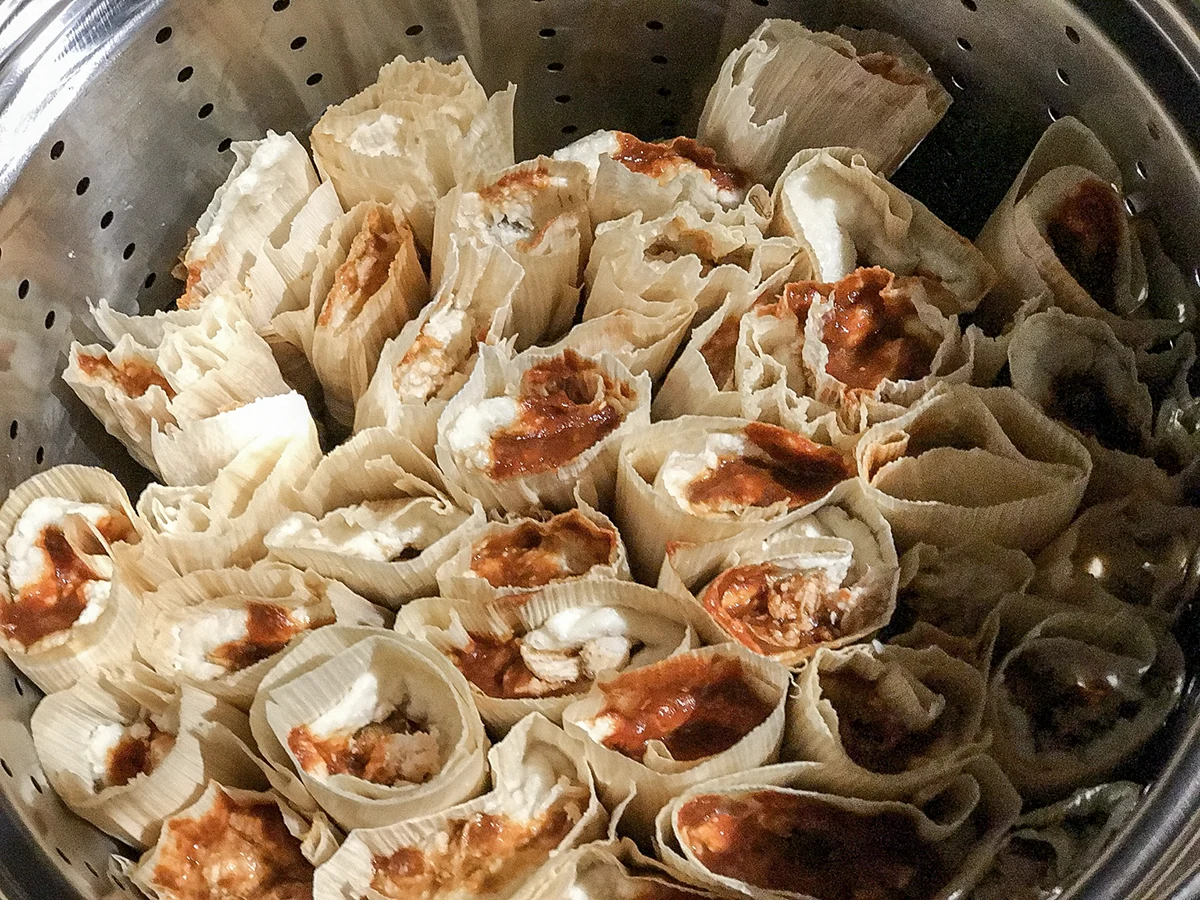 Corn-husk tamales arranged upright in a metal steamer.