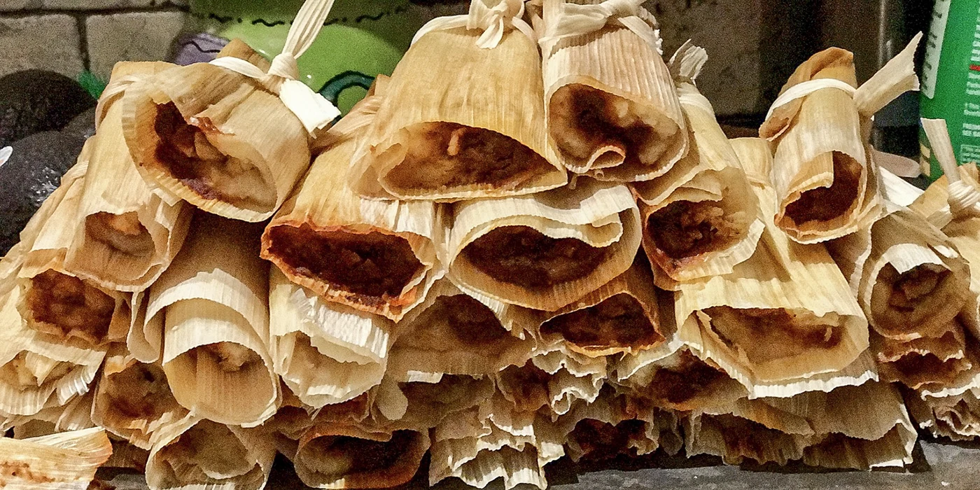 Wrapped tamales stacked on a tray.