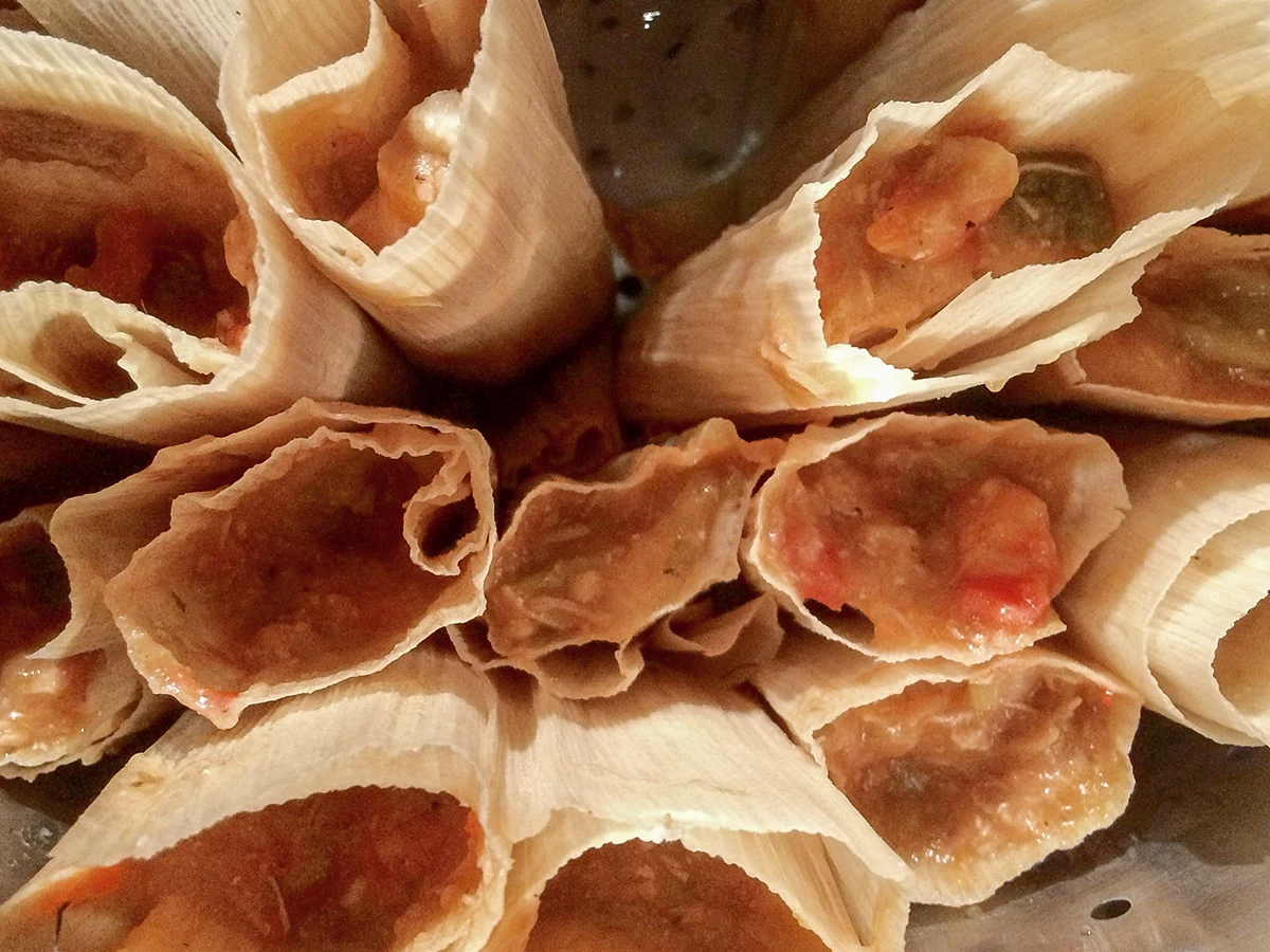 Corn-husk tamales arranged upright in a metal steamer.