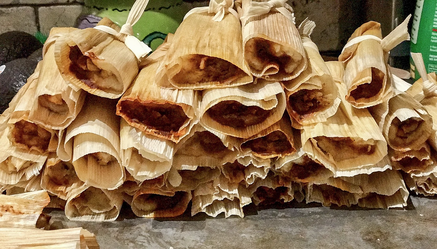 Wrapped tamales stacked on a tray.